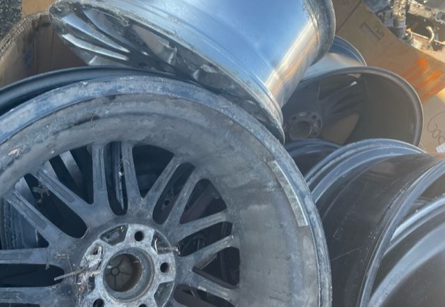 Piled car wheels and rims in a scrapyard, including a close-up black alloy wheel.