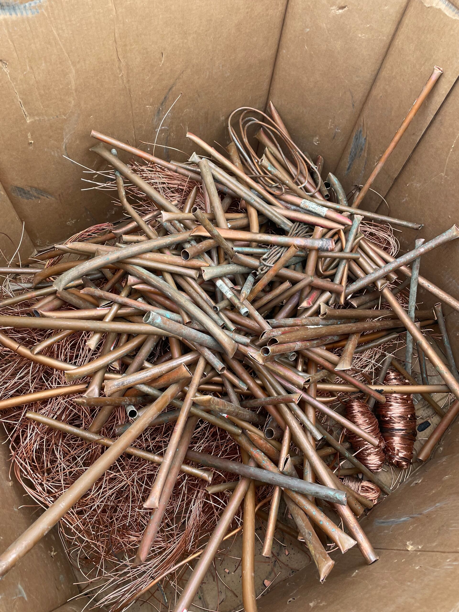 Cardboard box filled with bent copper tubing and metal rods with shiny copper debris