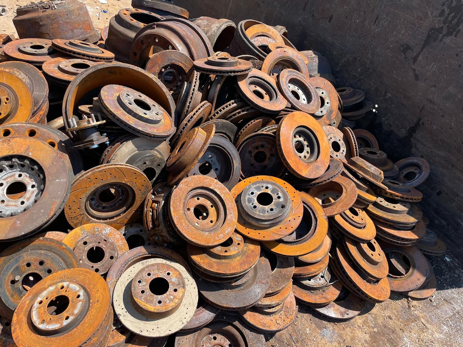 Pile of rusty metal brake rotors and wheels stacked in a scrap yard.