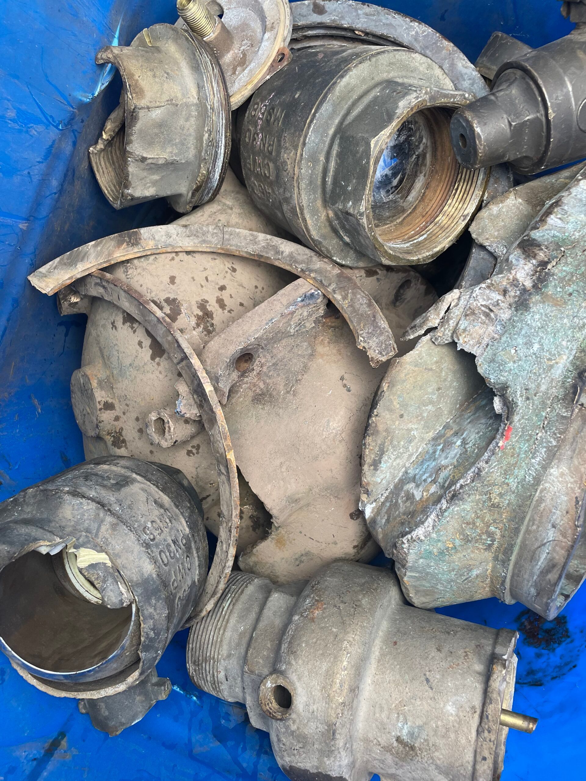 Assorted dusty metal pipe fittings and couplings piled in a blue container.