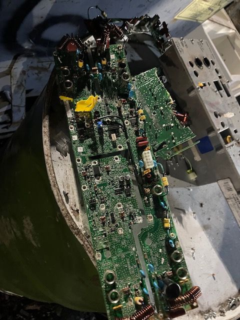 Damaged green circuit board with melted components inside a metal enclosure