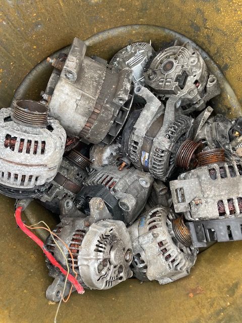 Pile of used metal alternators and motors in a bin, with a red wire visible in front.