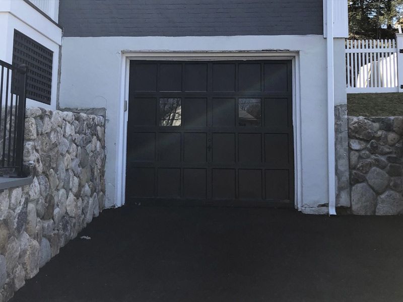 A black garage door is open next to a stone wall.