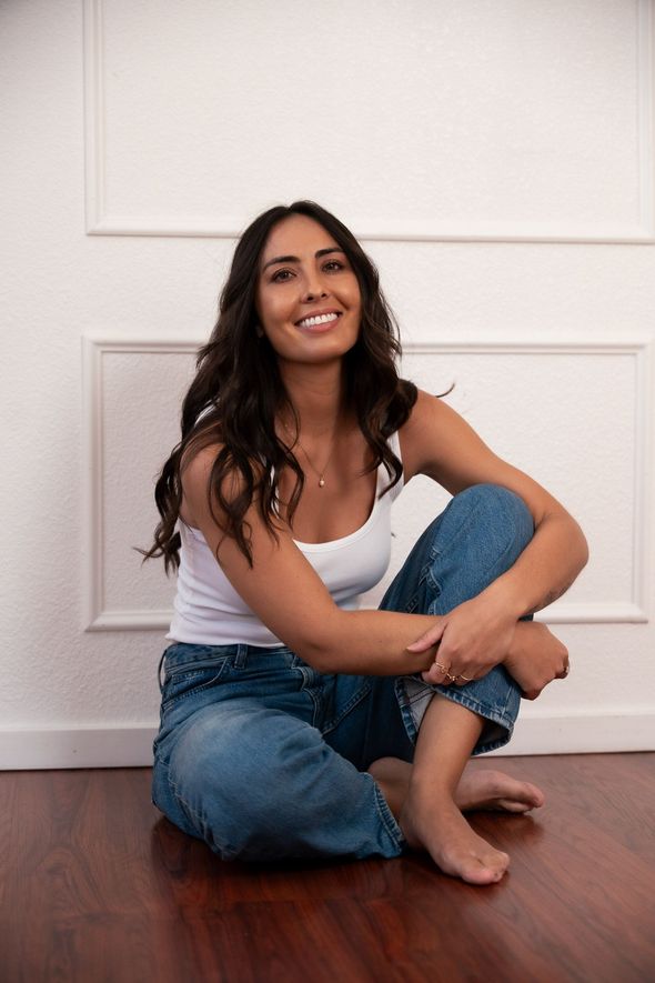 pmdd coaching in jeans and a white tank top sitting in front of a white wall