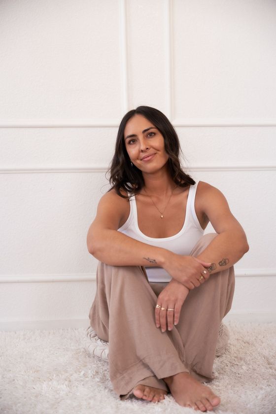 a pmdd coach in hawaii sitting in front of a white wall smiling at the camera
