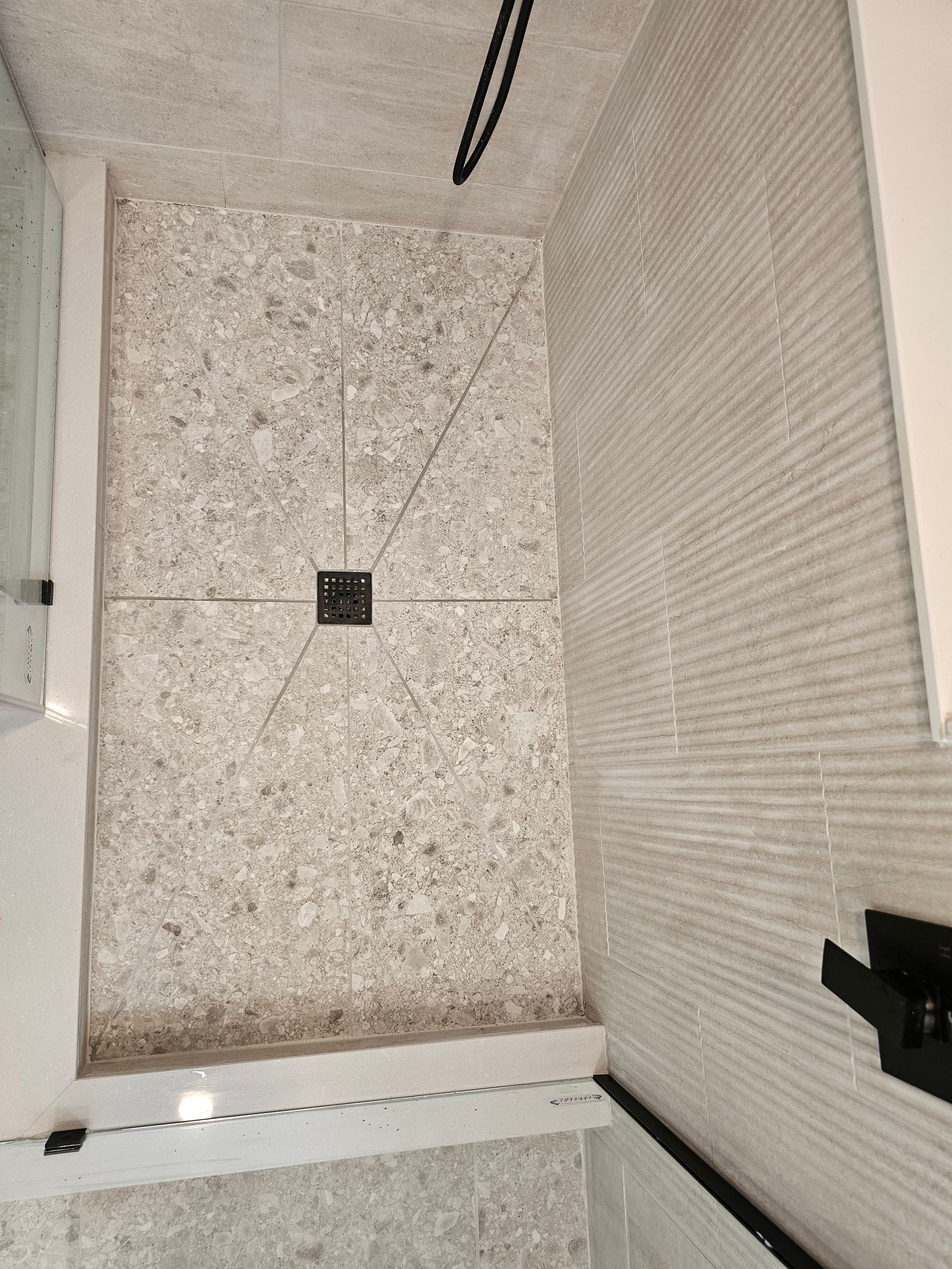 A bathroom with a walk in shower and a black railing.