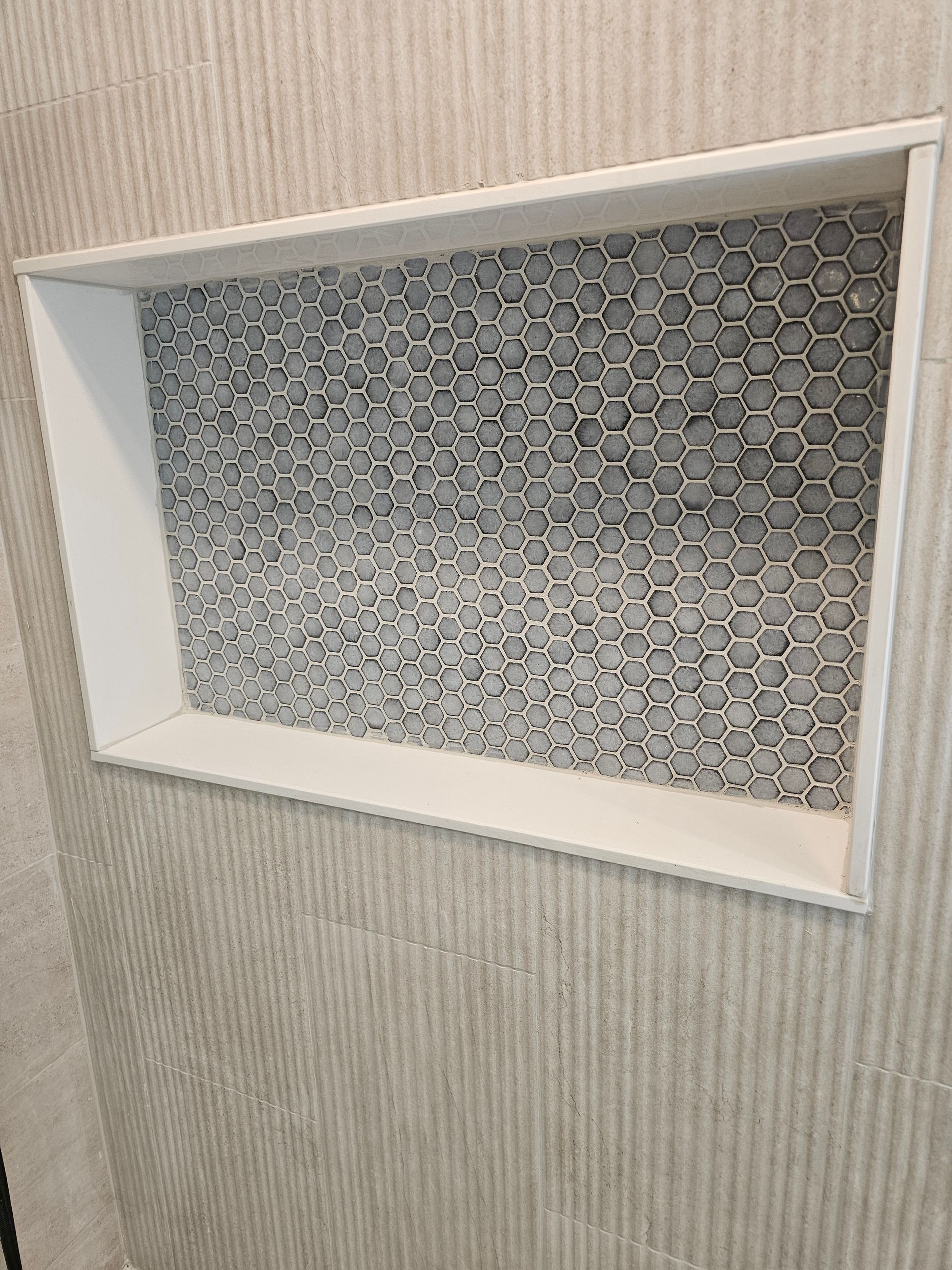 A shower niche in a bathroom with a gray tile wall.