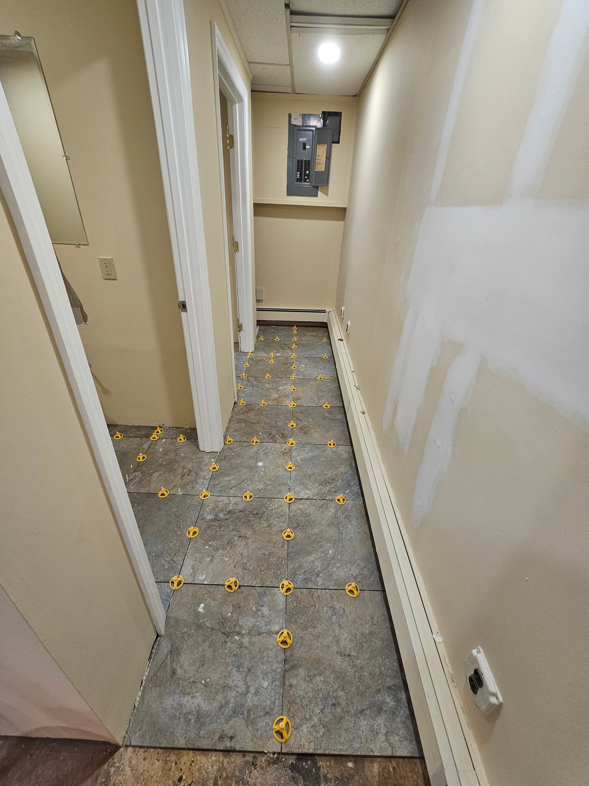 Hallway under construction with tile set in place, yellow leveling clips visible.