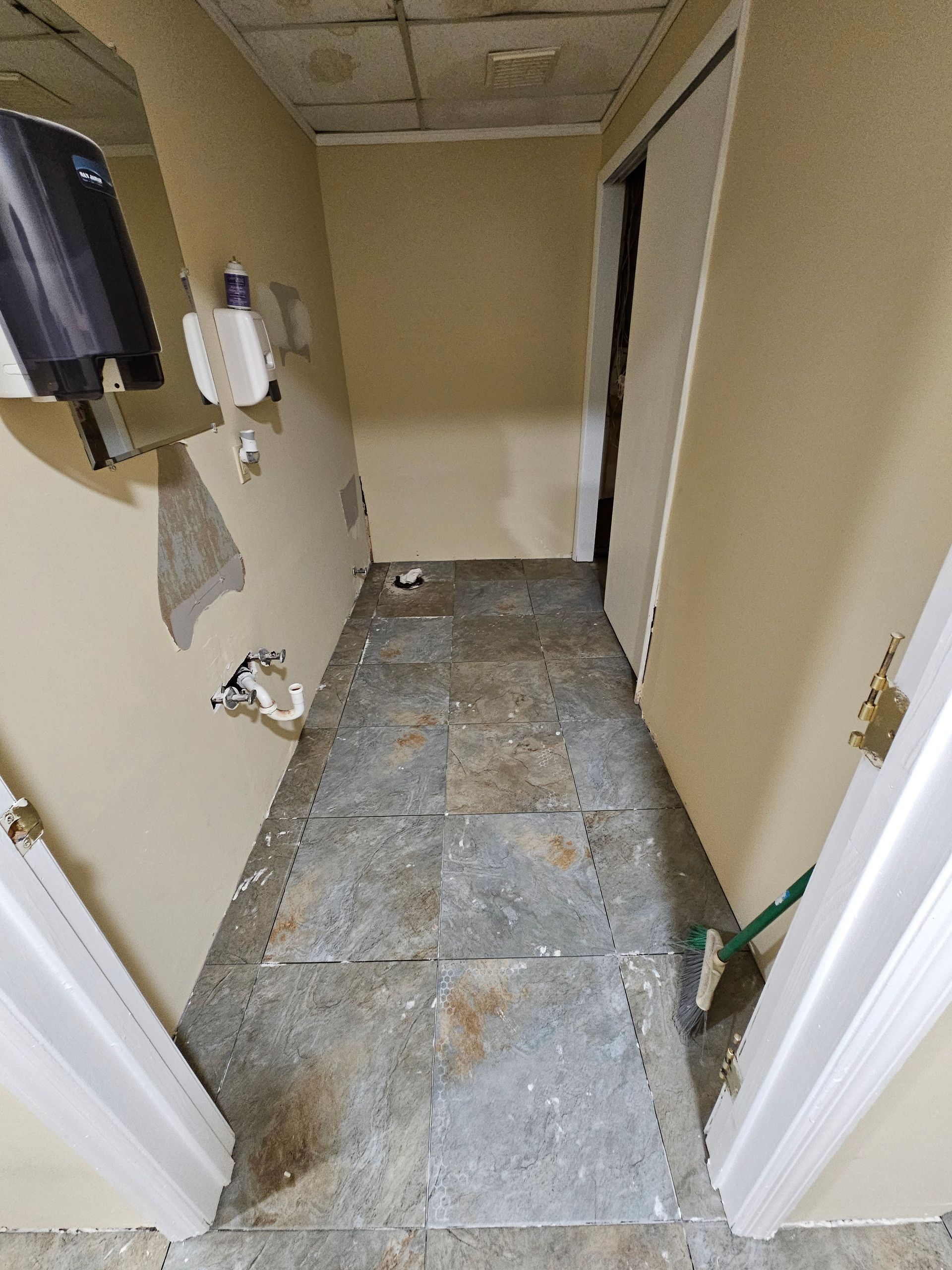 Narrow hallway with damaged walls, worn flooring, and a partially open closet door.