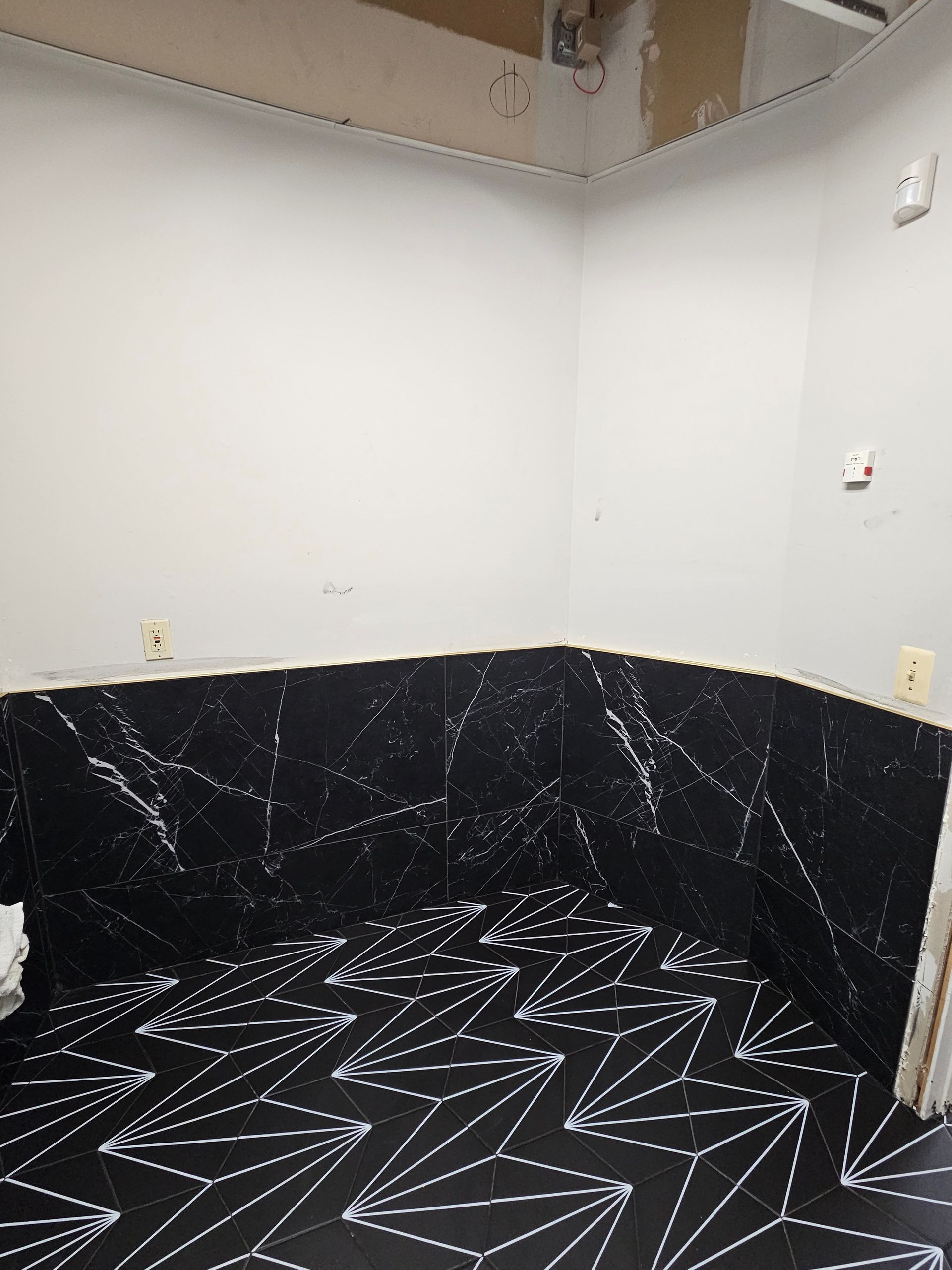 Room with black and white patterned tile floor and black marble-look wall. White walls overhead.