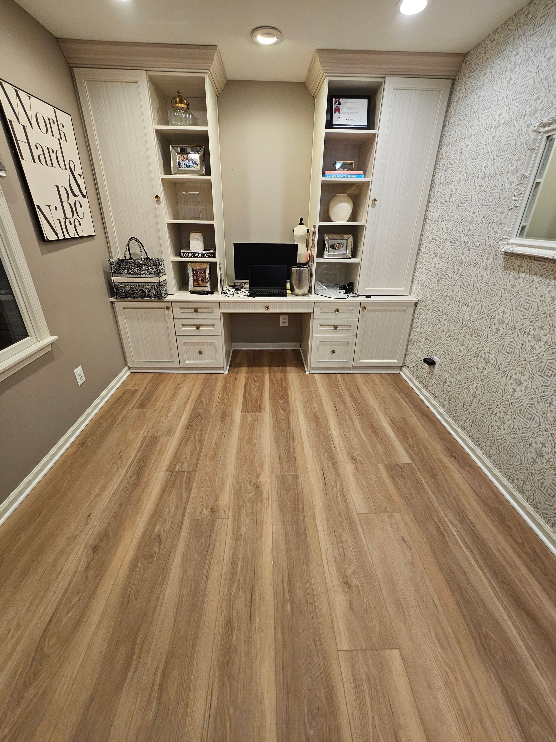 Home office with built-in desk and cabinets. Light wood floor, white desk and storage, neutral walls.