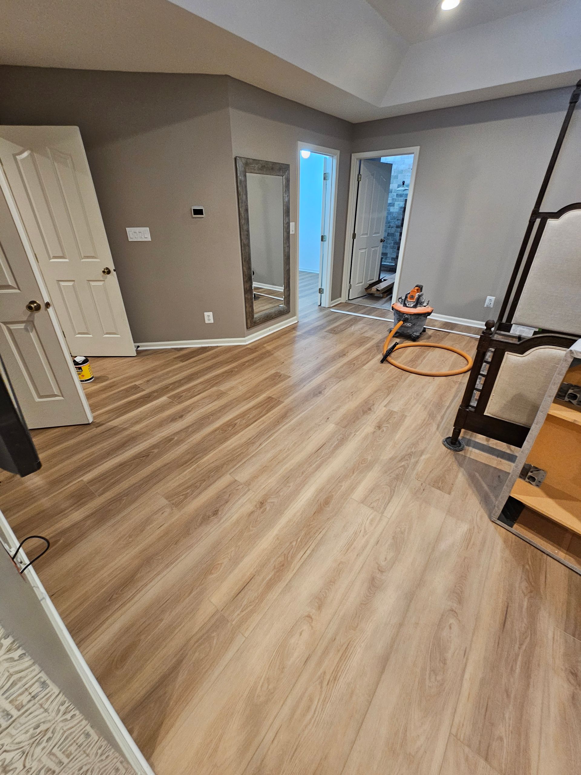 Newly installed wood-look flooring in a room with gray walls and doorways. A large mirror and equipment are visible.