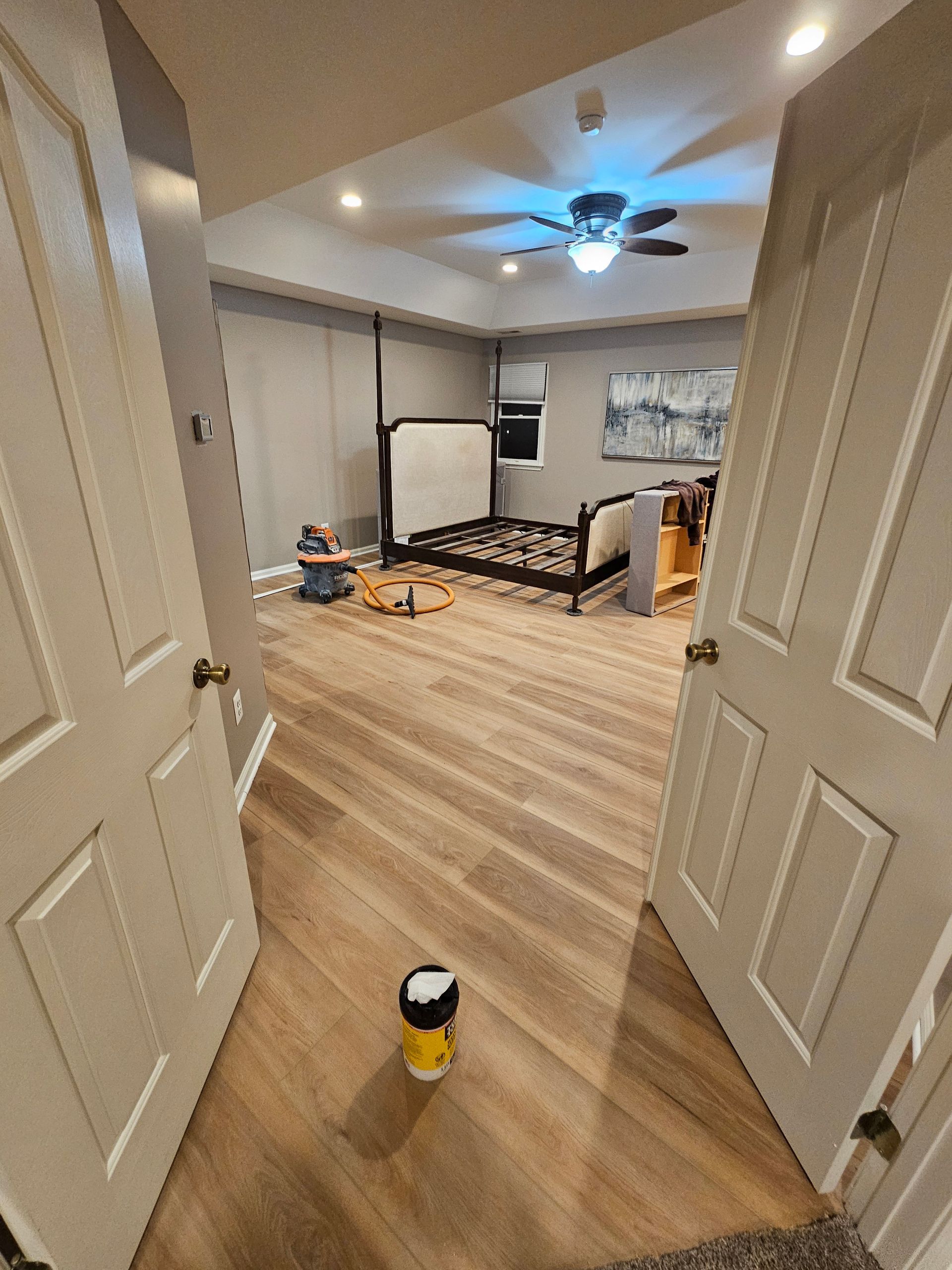 Open doorway looking into a bedroom with wood floors, a bed, and art. A small toy is on the floor in the foreground.