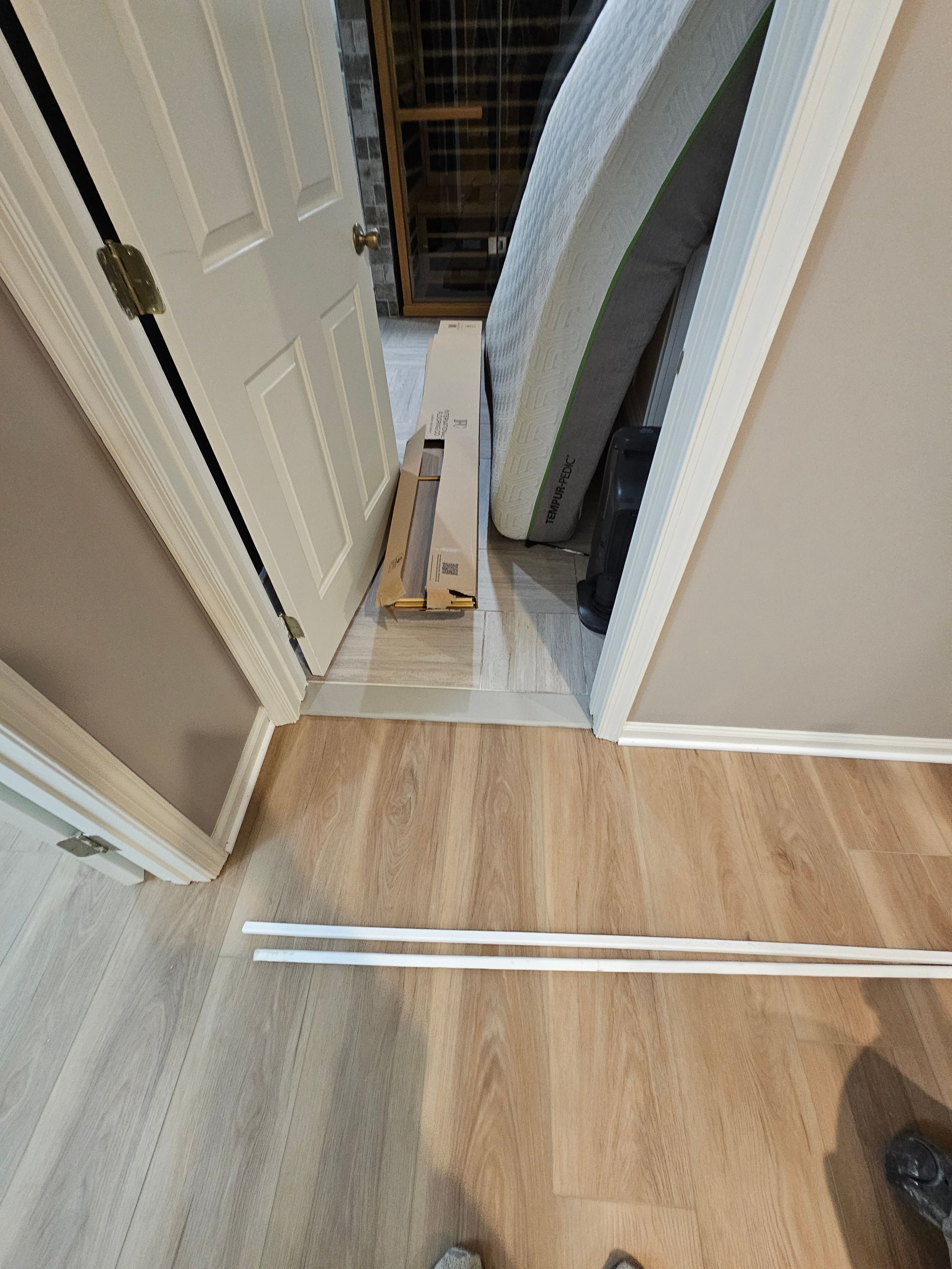 Ajar door with mattress and cardboard box blocking the doorway. Light wood-look flooring and white trim.