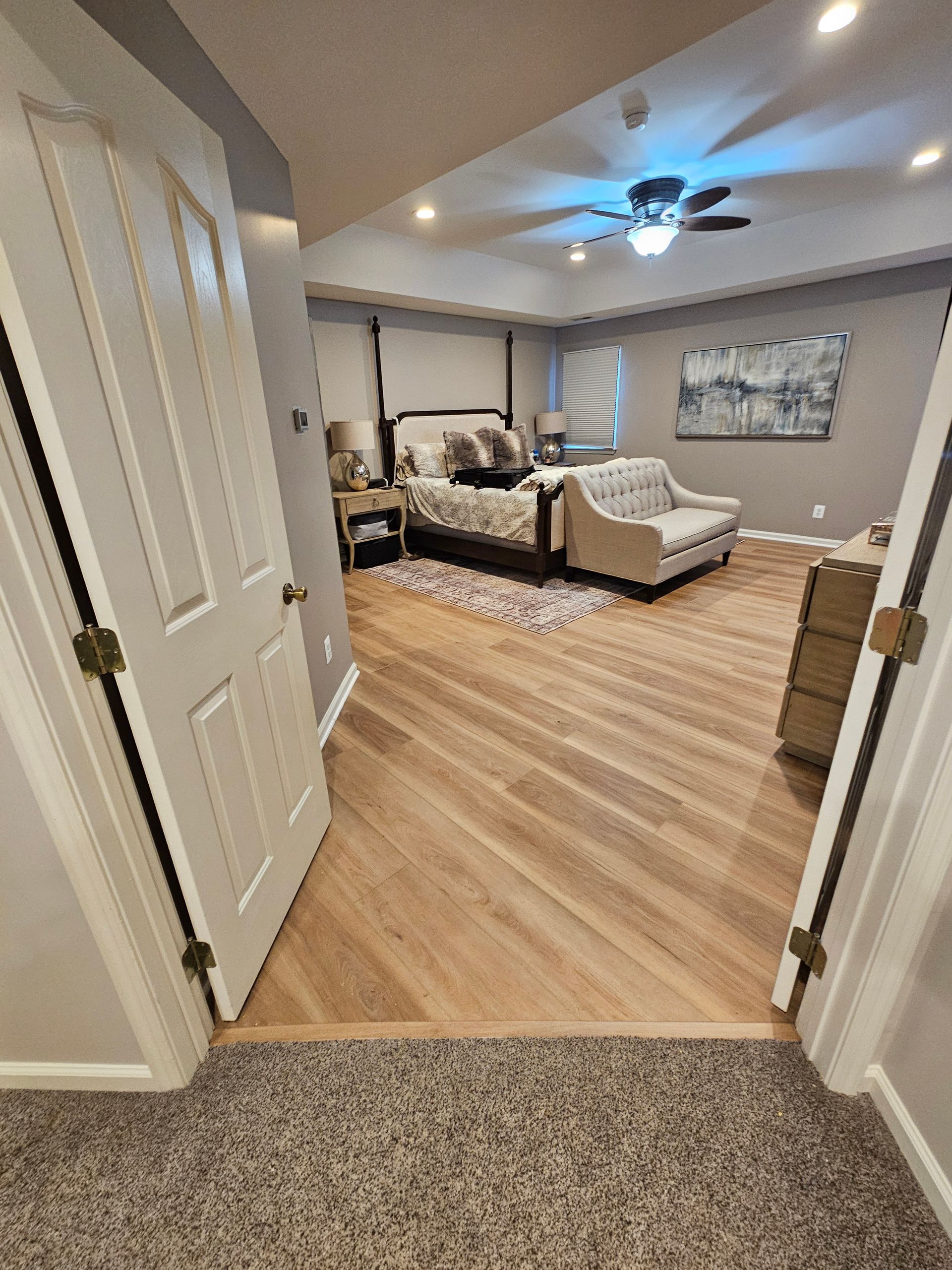 Bedroom with hardwood floor, bed, couch, and art; open doors in foreground.
