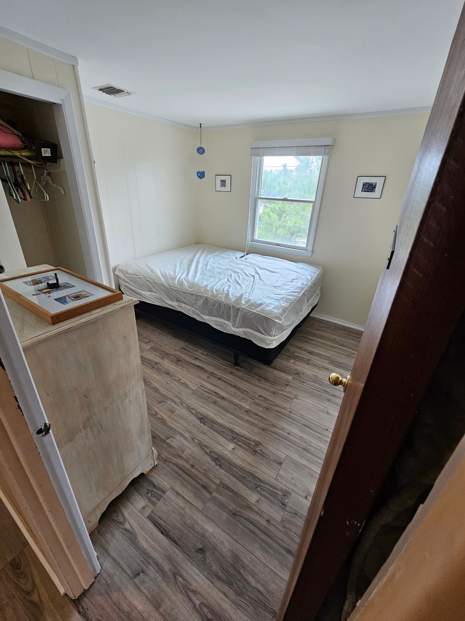 Bedroom with bed, dresser, window, closet. Light beige walls, wood-look floor, bed covered.