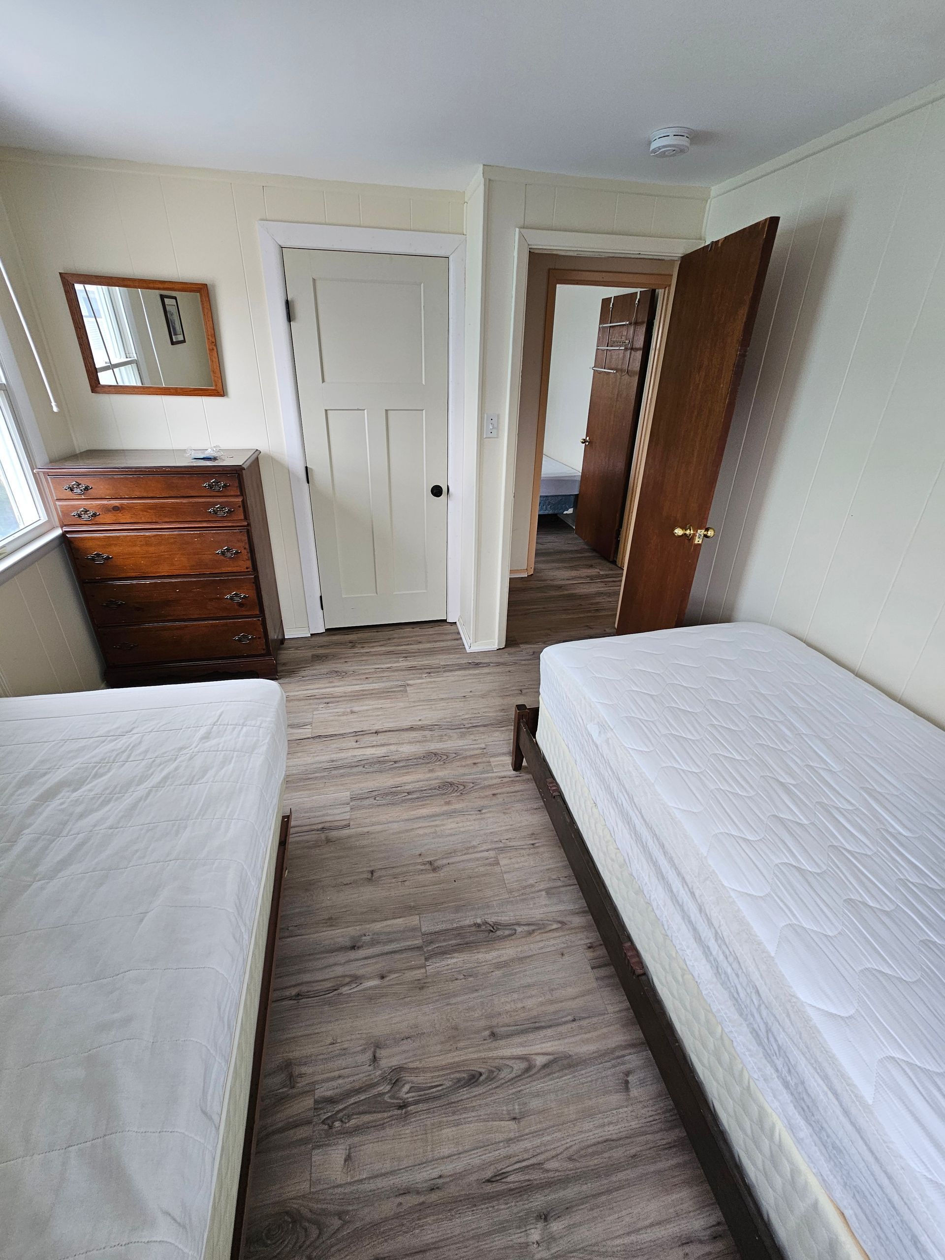 Bedroom with two twin beds, a dresser, and two open doorways. The walls are light.
