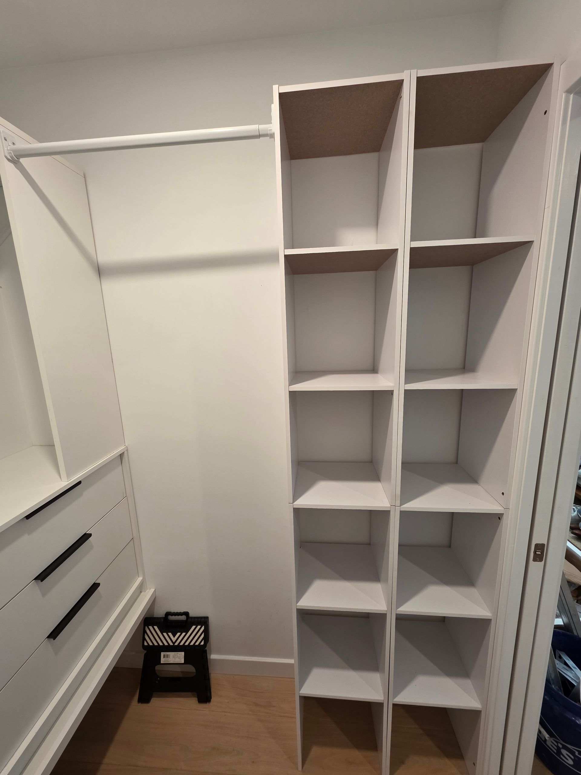 White closet organizer with shelves and hanging rod. Black handles on drawers.