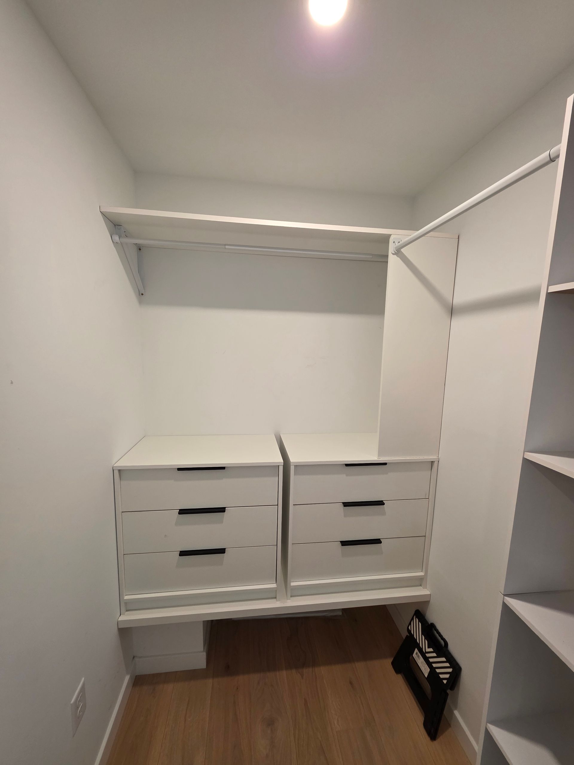 White walk-in closet with drawers and shelves. Light wood-look flooring.