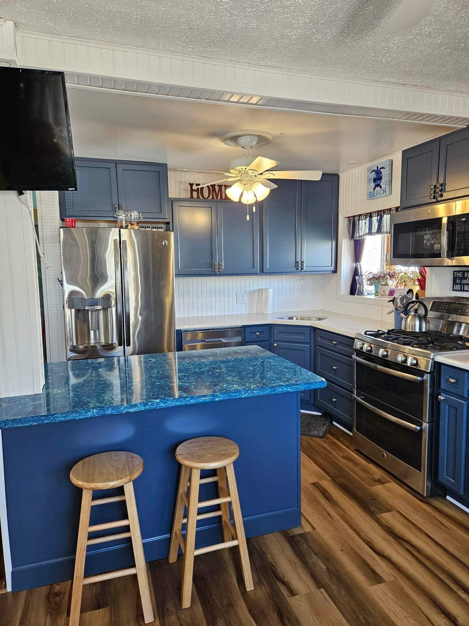 Blue and stainless steel kitchen with a blue island and wooden stools.