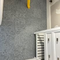Gray penny tile wall, white cabinetry, yellow hose.