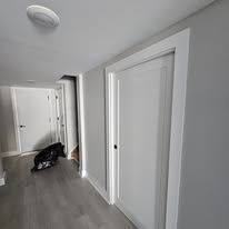 White hallway with a closed white door and a trash bag on the floor.