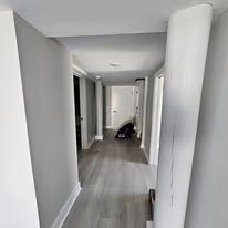 Long, gray hallway with wood floors and doorways, dark object at end.