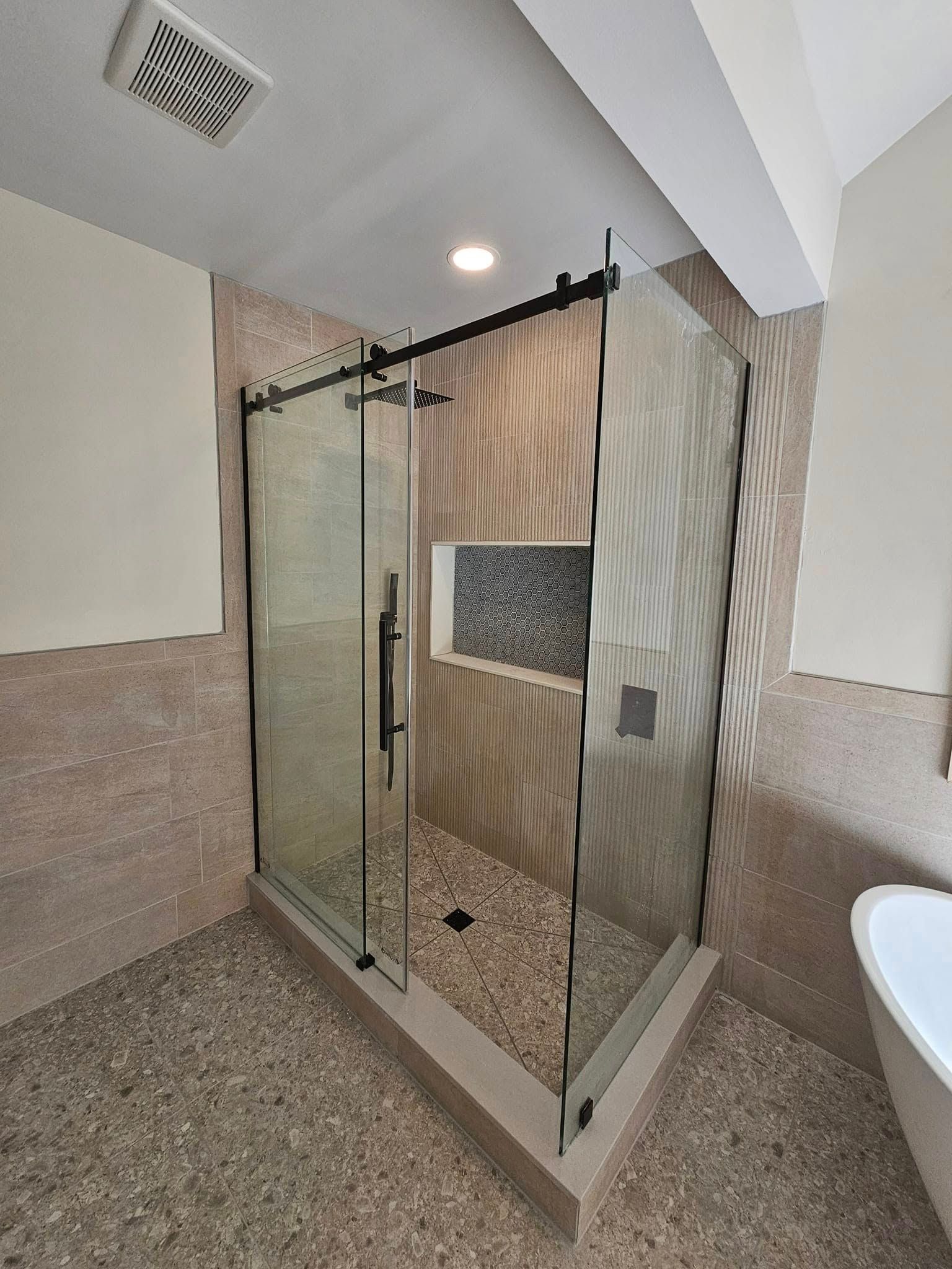 Modern shower with glass doors, pebble floor, stone walls, and black hardware.