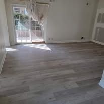 Empty room with light gray wood-look flooring, large windows, and a sheer curtain.