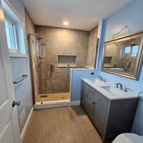 Bathroom with a shower, vanity, and large mirror. Light wood floors and tile walls.