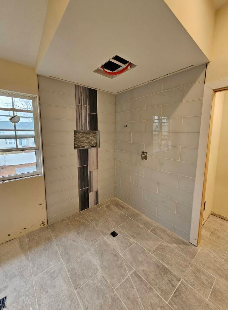 Bathroom with tiled walls and floor, shower area with decorative accents, and a window.