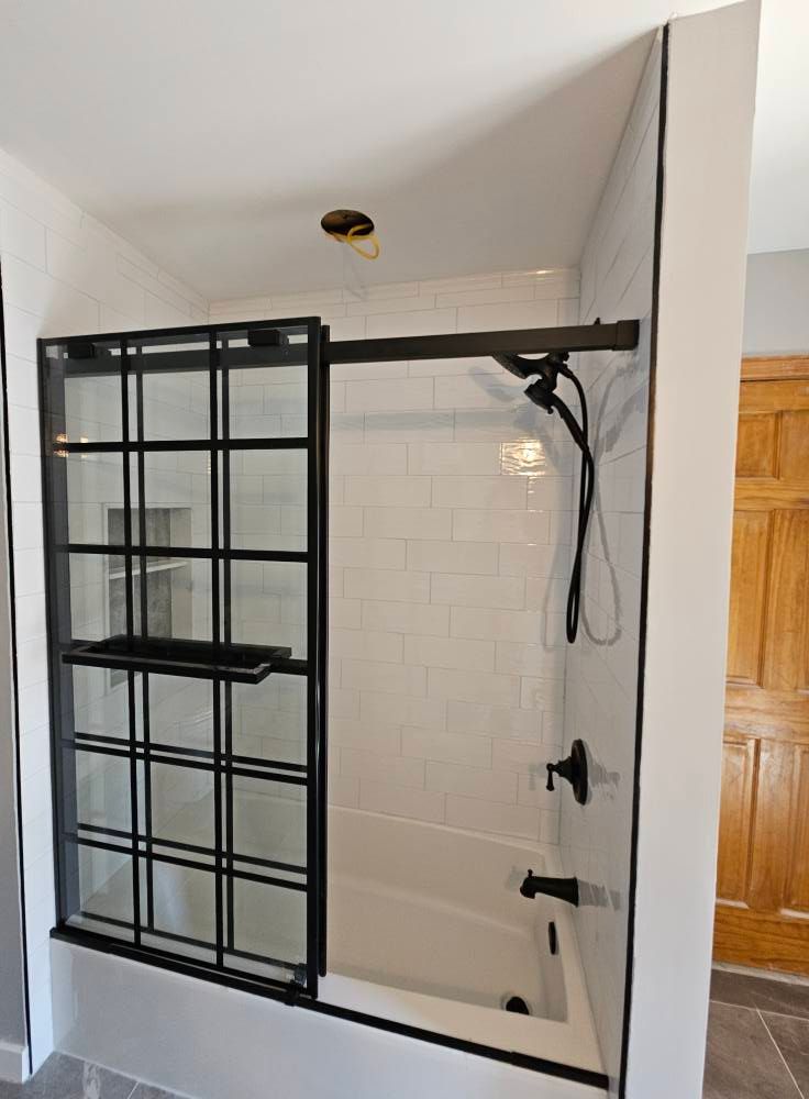 Black-framed shower with sliding door over a white tub and subway tile. Black shower fixtures.