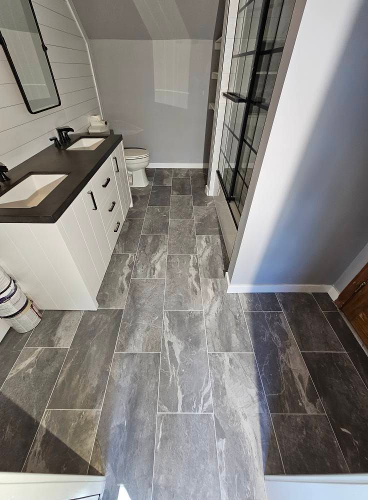 Bathroom with gray tile floor, white vanity with black fixtures, and a tall window.