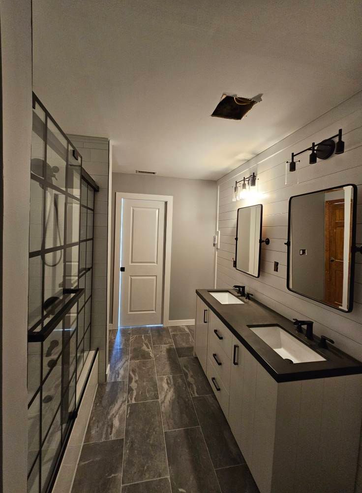 Bathroom with gray tile floor, white shiplap wall, double vanity, and black framed shower.