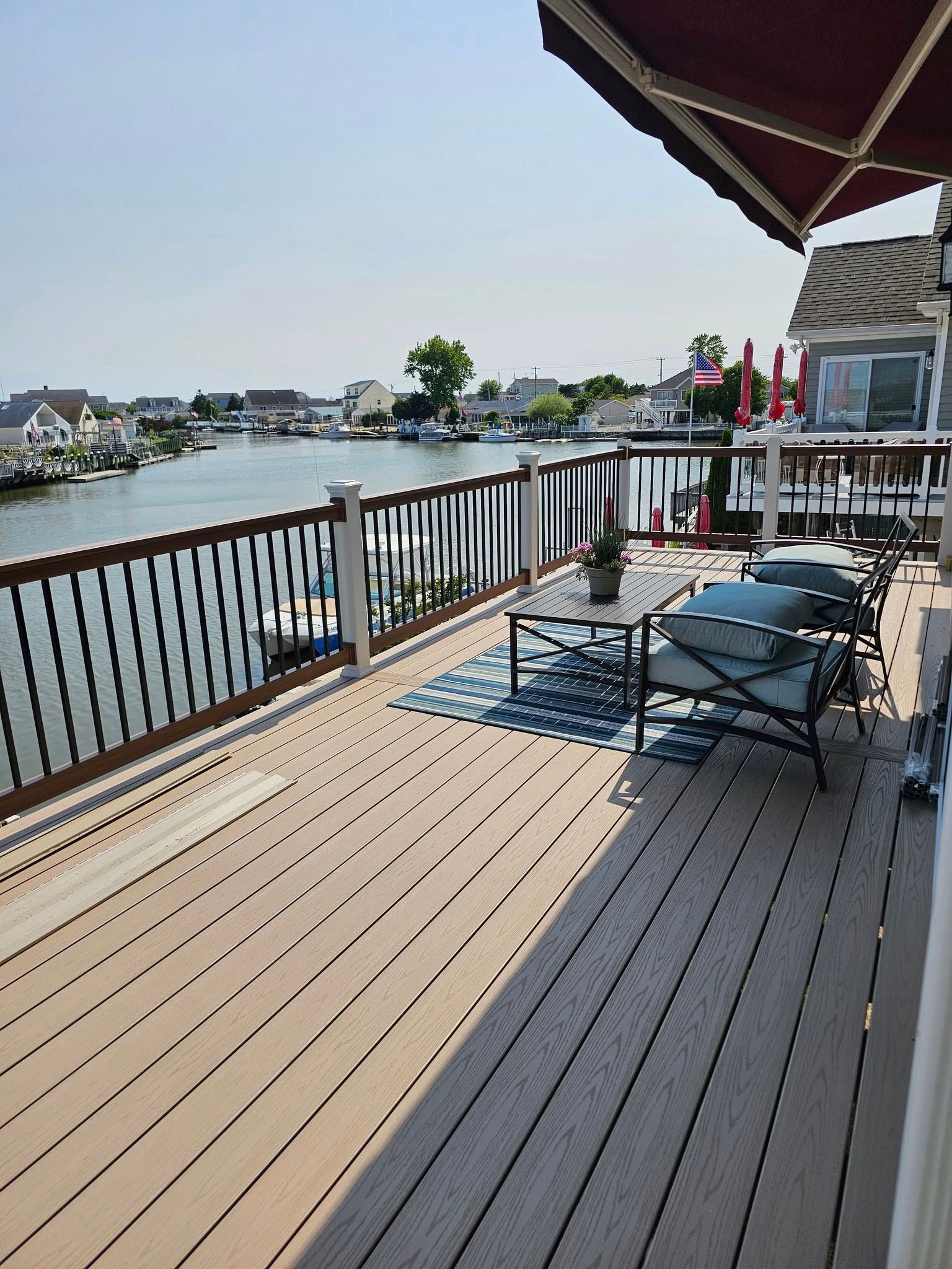Wooden deck overlooking a waterway with boats, outdoor furniture, and a red awning.