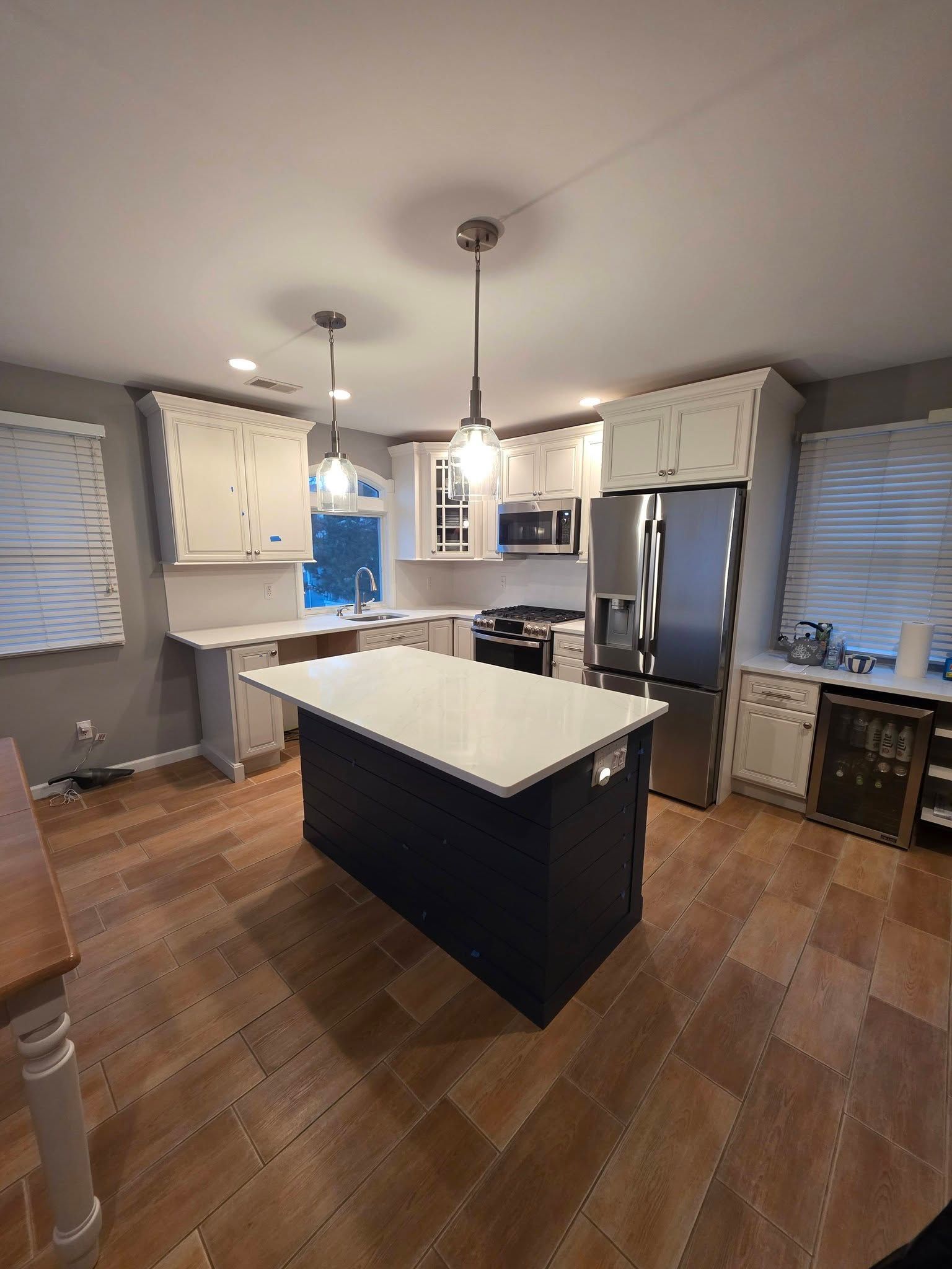 Kitchen with dark blue island, white cabinets, stainless steel appliances, and wood flooring.
