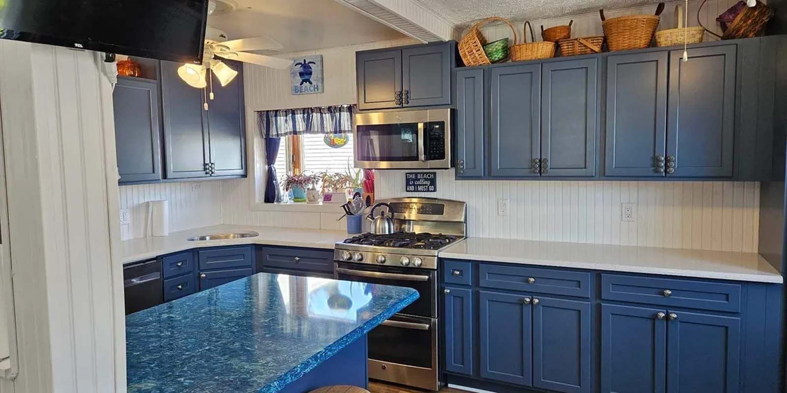 A kitchen with blue cabinets , a stove , a microwave , and a sink.