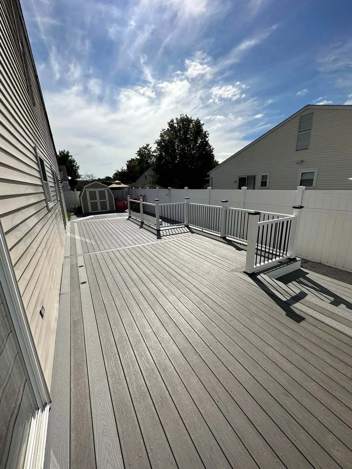 A large wooden deck with a white railing in front of a house.