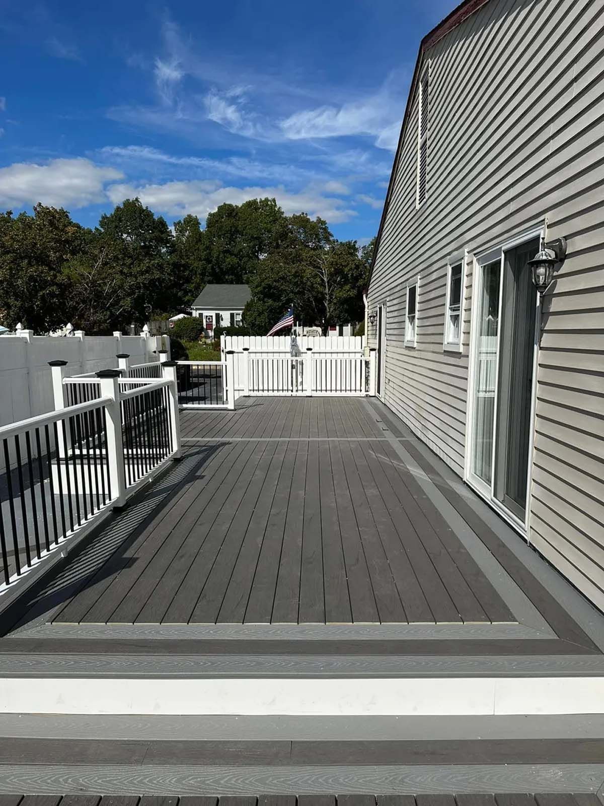 A large deck with a white railing and sliding glass doors on the side of a house.