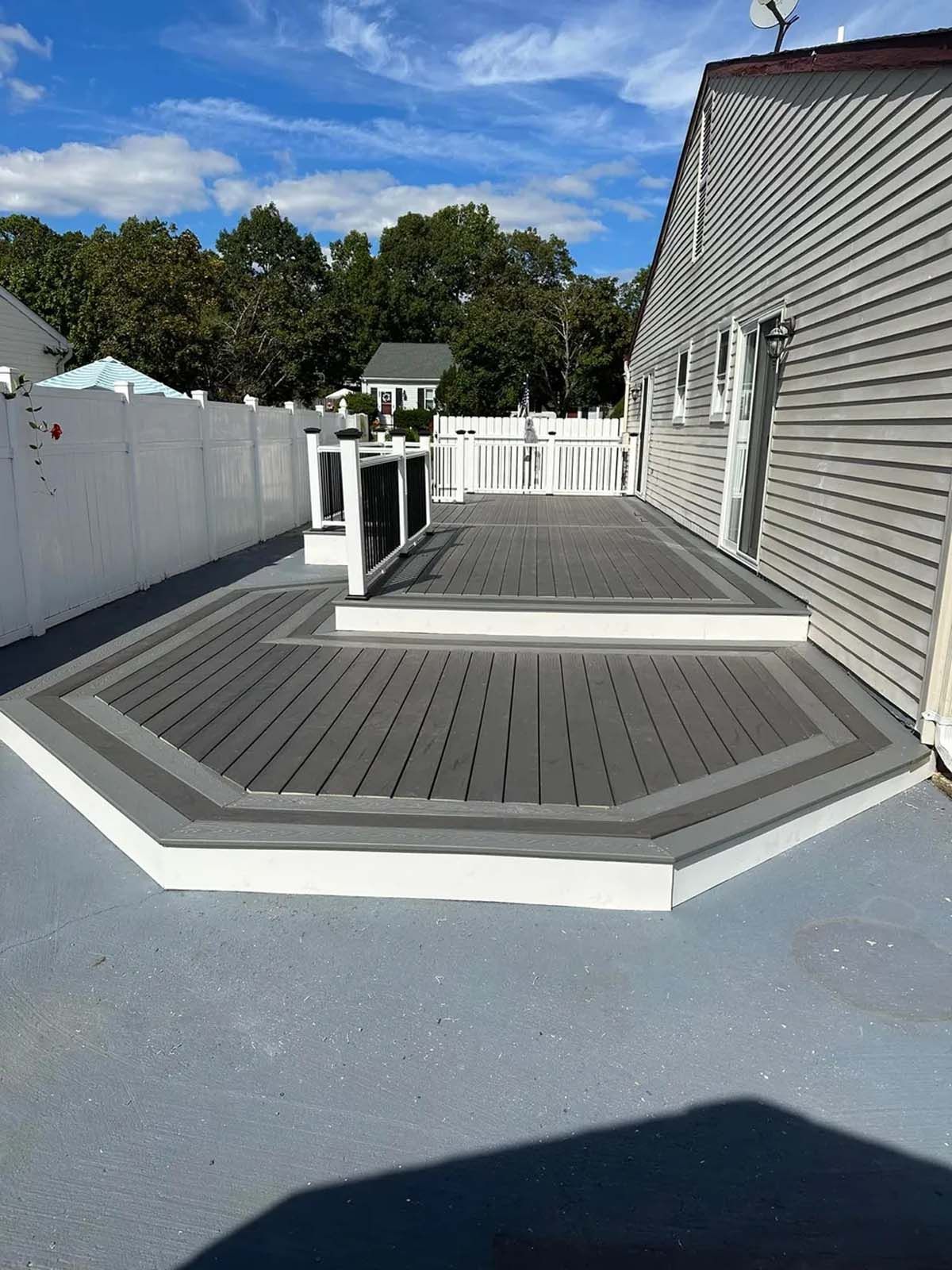 A gray and white deck with a white fence in front of a house.
