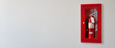 Red fire extinguisher in a wall-mounted cabinet on a light gray wall.