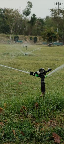 Sprinkler spraying water over a grassy field with trees in the background