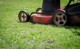 Close-up of a red lawn mower on green grass, with black and silver wheels.