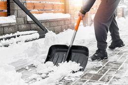 Person shoveling snow from a brick walkway with a black snow shovel and orange handle