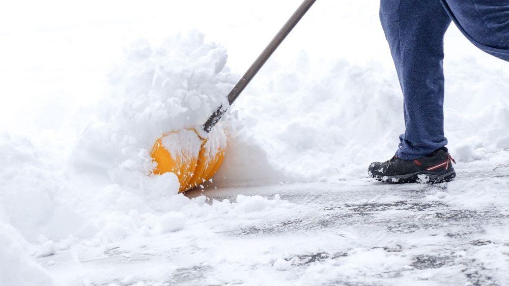 Person shoveling snow with an orange shovel beside a sidewalk