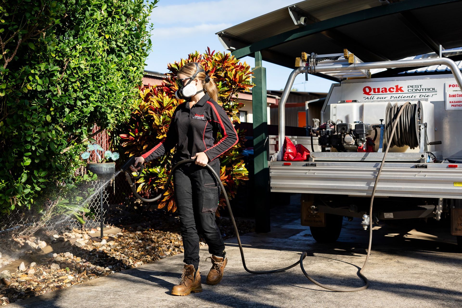 Woman Spraying With a Hose Near a Truck; Wearing a Mask and Work Clothes — Quack Pest Control in Berrimah, NT
