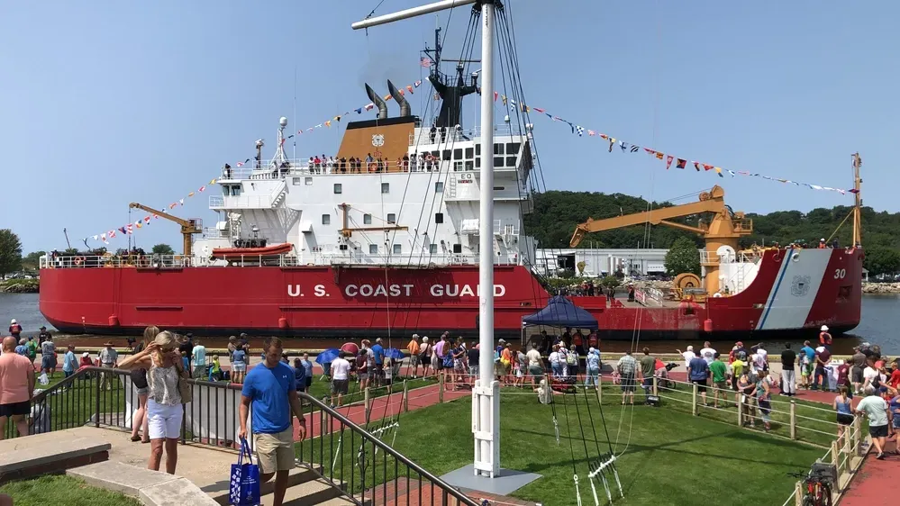 Large U.S. Coast Guard ship on display by a waterfront crowd on a sunny day