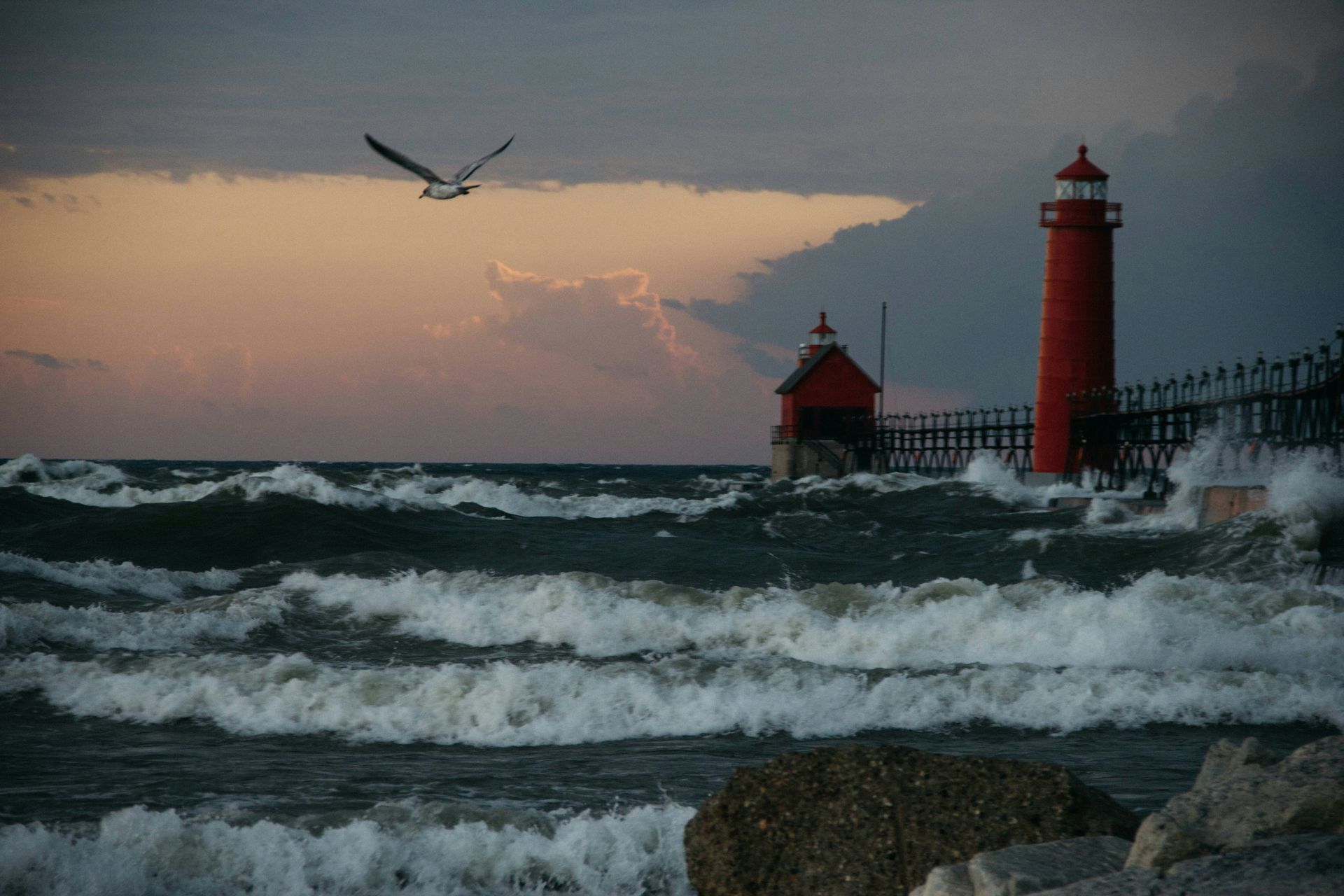 Red lighthouse and rough ocean waves at dusk, with a bird flying overhead.