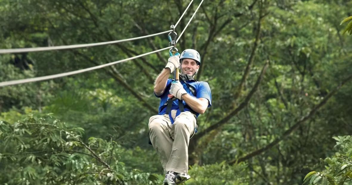 A man wearing safety gear while ziplining through a forest