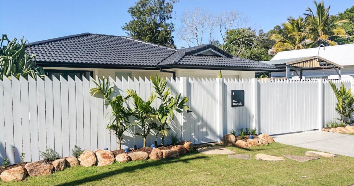 A White Fence Surrounds a House with A Black Roof — Byron & Beyond Fencing In Billinudgel, NSW